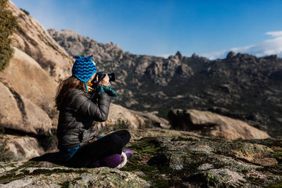 Man photographing rock on mountain against sky