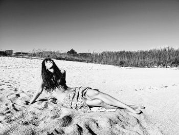Woman relaxing on beach against clear sky