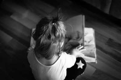 High angle view of girl reading book while sitting on floor at home