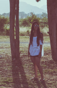 Smiling young woman standing by trees on field