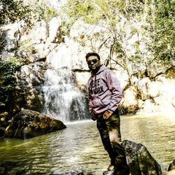 Man standing on rock against waterfall in forest