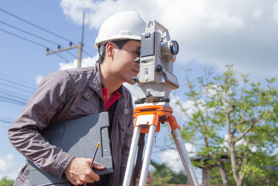 Side view of engineer looking through theodolite at construction site
