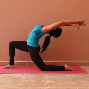 Young woman practicing yoga on mat against wall