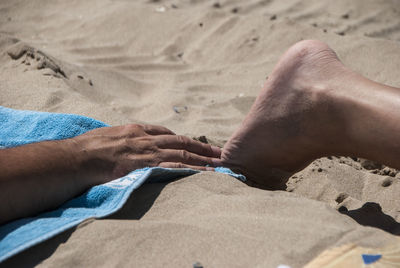 Low section of man relaxing on sand at beach