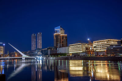 Puente de la mujer over river in illuminated city against clear sky at dusk