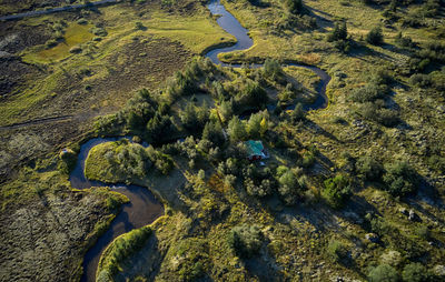 Magnificent view of solitary cottage near winding river crossing meadow through small green forest in sunny summer day