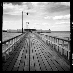 Walkway leading to sea against cloudy sky