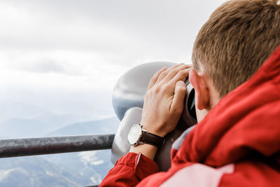 Young blond man looks at mountain views in binoculars from observation