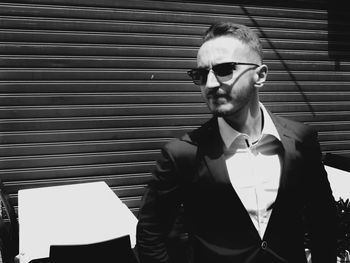 Portrait of young man wearing sunglasses standing against wall