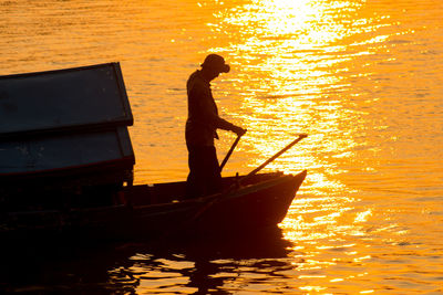 Silhouette mature man standing in boat on sea during sunset