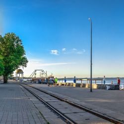 View of railroad tracks by street against blue sky