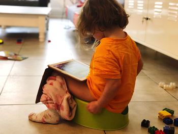 Girl using digital tablet while sitting on toilet bowl at home