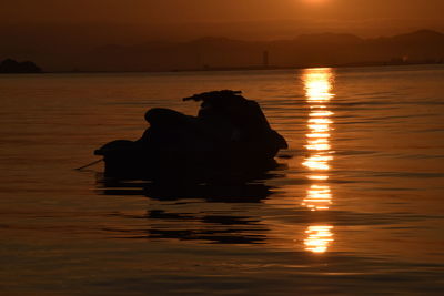 Silhouette men by sea against sky during sunset