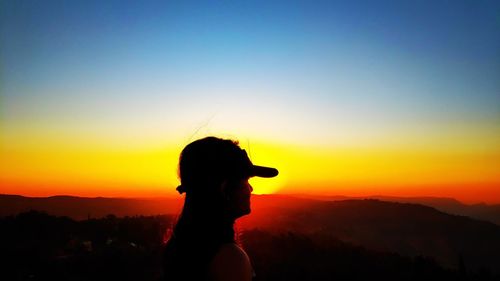 Silhouette woman looking at view against dramatic sky during sunset