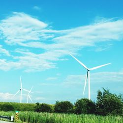 Wind turbines on grassy field against cloudy sky