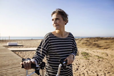 Woman with bicycle at beach against clear sky