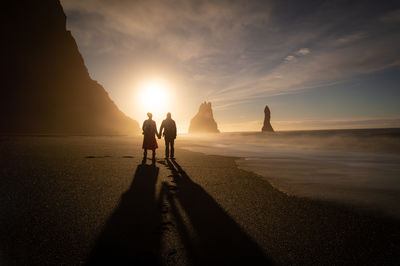 Silhouette people walking on beach against sky during sunset