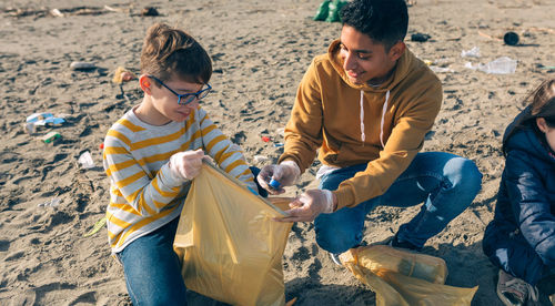 Young man with kids picking garbage from beach