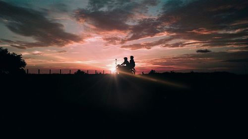 Silhouette friends on motorcycle against sky during sunset