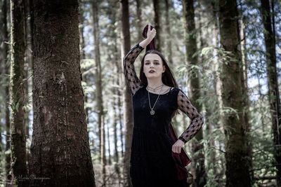 Woman standing by tree trunk in forest