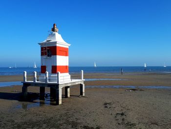 Lighthouse on beach against clear blue sky