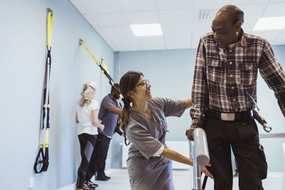 Smiling female caregiver helping senior man to walk at nursing home