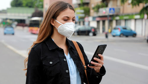 Woman wearing mask using mobile phone while standing on street