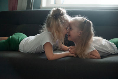 Cute girl touching noses while lying down on sofa at home