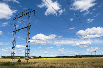 Electricity pylons and wind turbine against blue sky