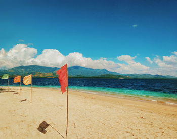 Flags on sand at beach against blue sky