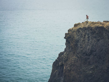 Man standing on cliff by sea fishing