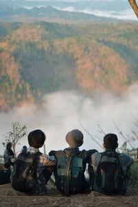 Rear view of people sitting on land against mountains