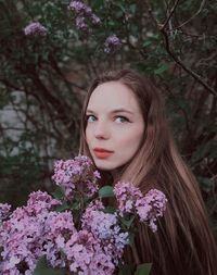 Portrait of beautiful young woman with pink flower against trees