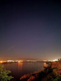 Illuminated city by river against sky at night