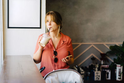 Young woman using mobile phone at local coffee shop while drinking cold beverage