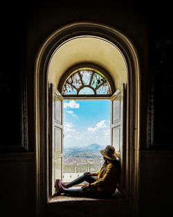 Rear view of woman sitting on window