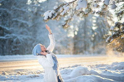 Happy laughing blonde woman in a white coat, a blue scarf and hat walks through the forest 