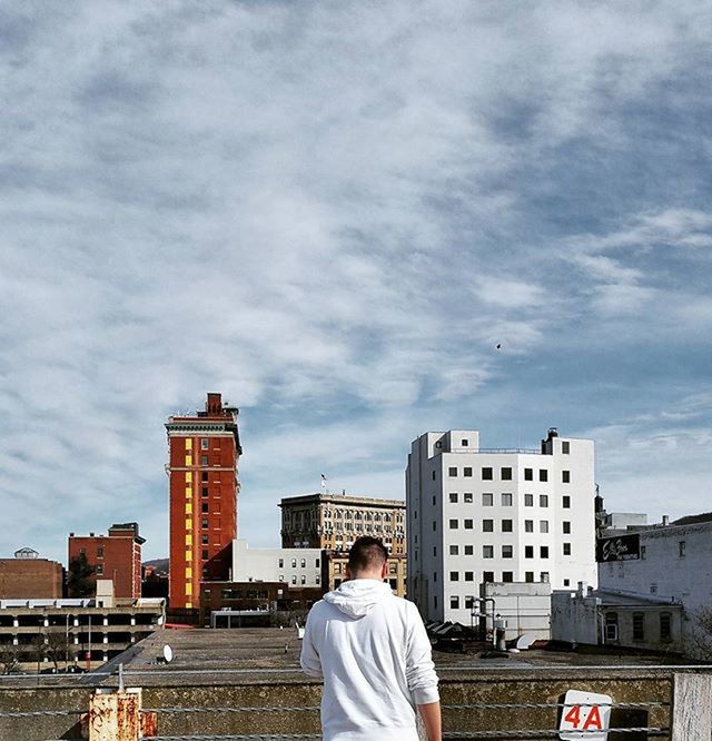 building exterior, built structure, architecture, city, sky, lifestyles, skyscraper, men, modern, cloud - sky, city life, rear view, leisure activity, railing, office building, building, standing, cityscape