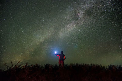 Rear view of man with illuminated flashlight standing against star field