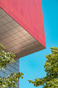 Red angular building against blue sky and trees 