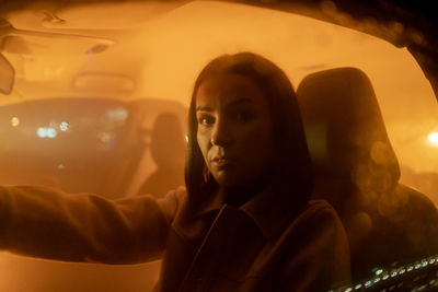 Portrait of serious woman enjoying night drive while sitting in car and looking at the camera