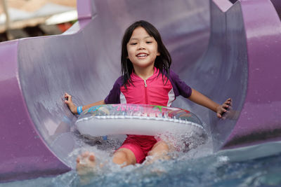 Portrait of happy girl sliding down in water slide at water park