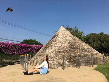 Woman sitting on land by built structure against clear sky