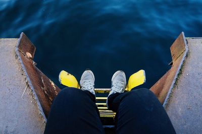 Low section of man sitting on pier over sea