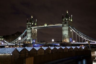 Illuminated bridge over river against sky in city at night