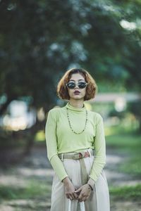 Portrait of young woman wearing sunglasses while standing on land against trees