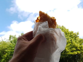 Close-up of hand holding ice cream against sky