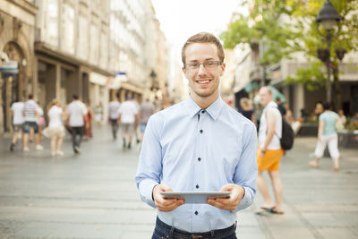 Portrait of young man holding smart phone standing in city