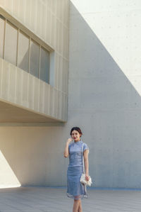 Portrait of young woman standing against building