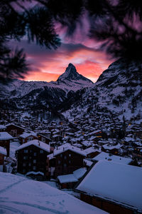 Snow covered houses and mountains against sky during sunset